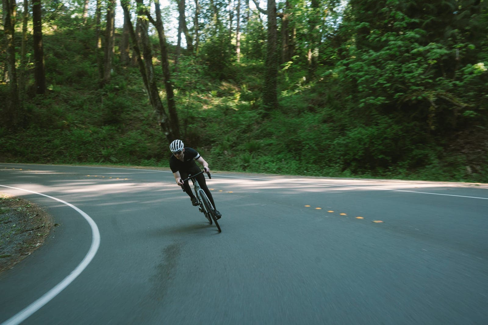 Jordan cornering on a road bike along a forested road
